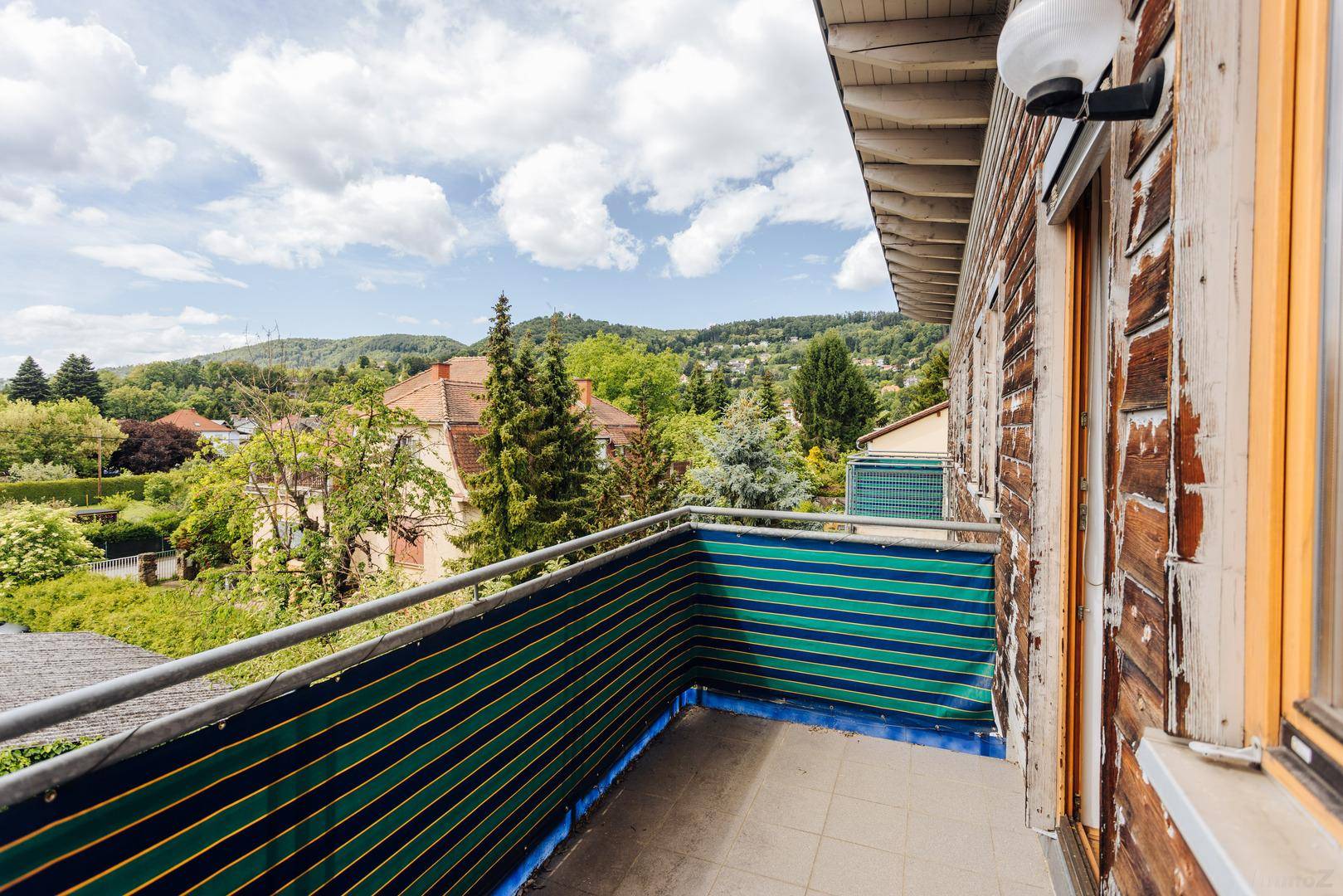Kleiner Balkon mit grüner Sichtschutzwand und weitem Blick über die hügelige Landschaft.