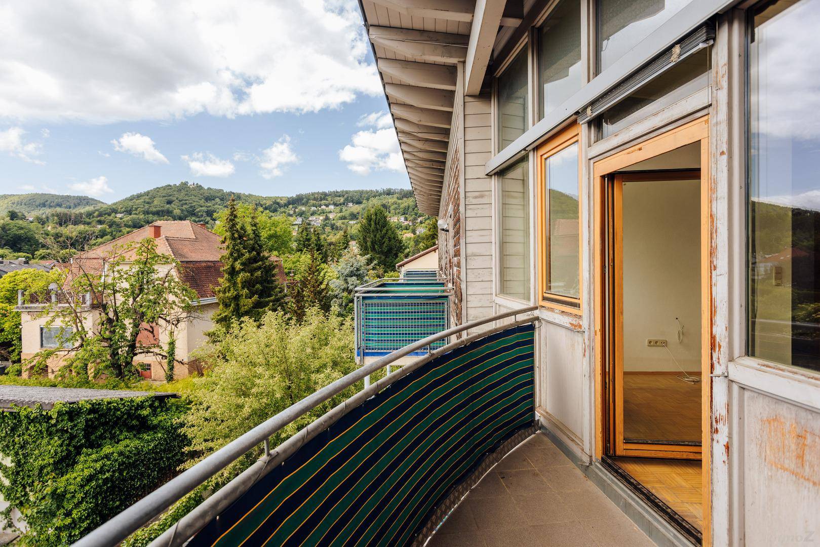 Gebogener Balkon mit Metallgeländer und weitem Blick über die grüne Umgebung und Häuser.