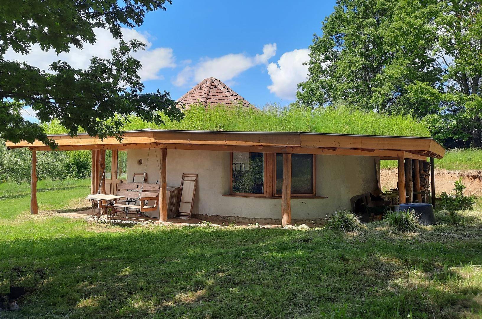 Außenseite eines Gebäudes mit begrüntem Dach, Holzstützen und einer kleinen Terrasse.