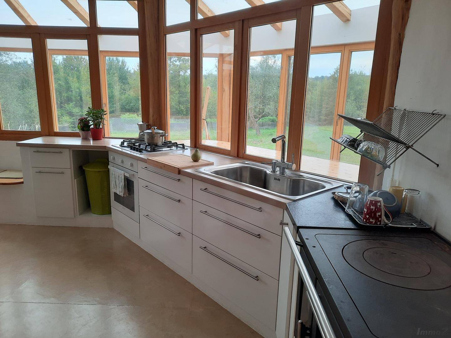 Helle Küche mit Spüle, Herd und großen Fenstern mit Blick ins Grüne.