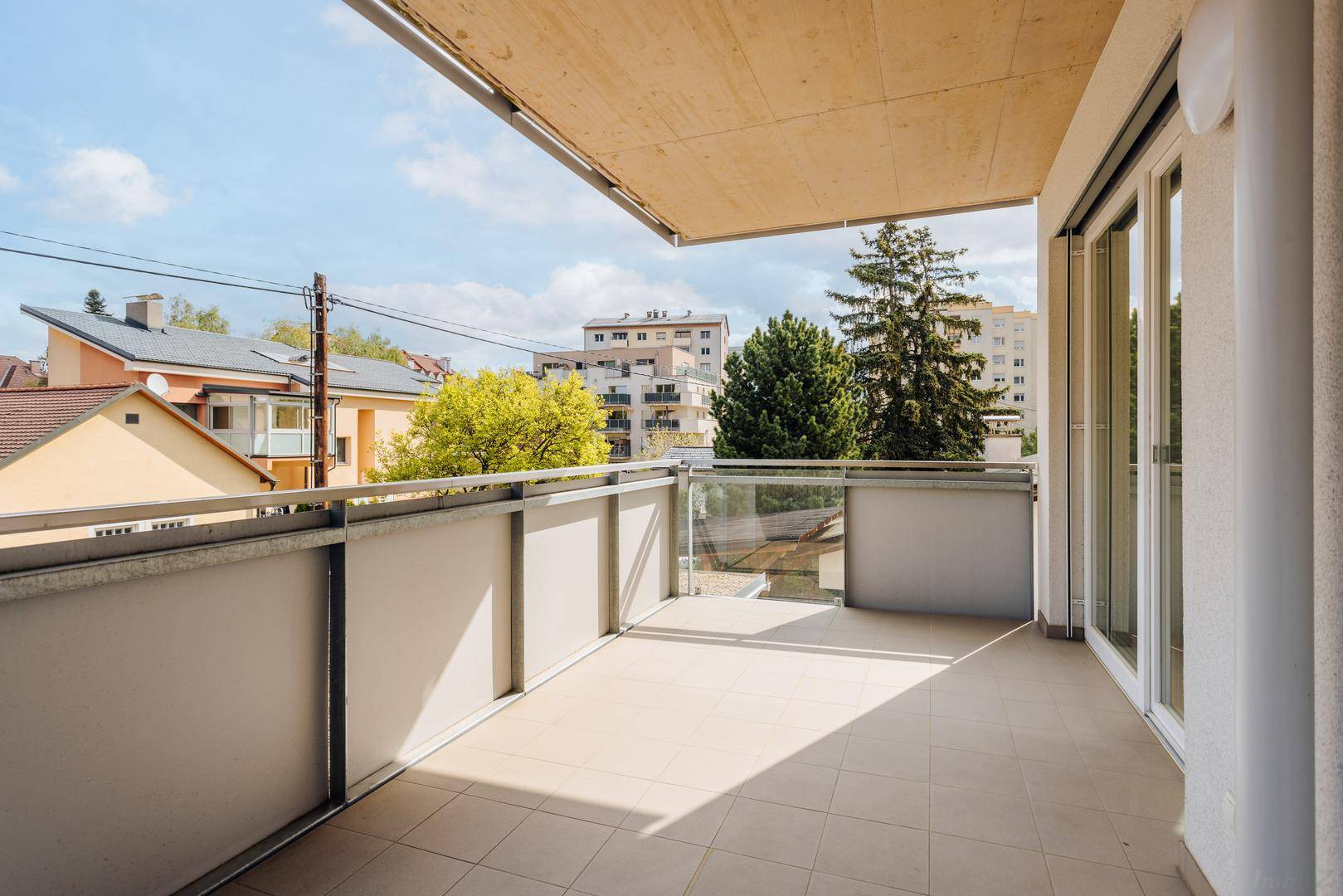 Geräumiger Balkon mit Fliesenboden und Glasgeländer, bietet einen Blick auf die umliegende Wohngegend.