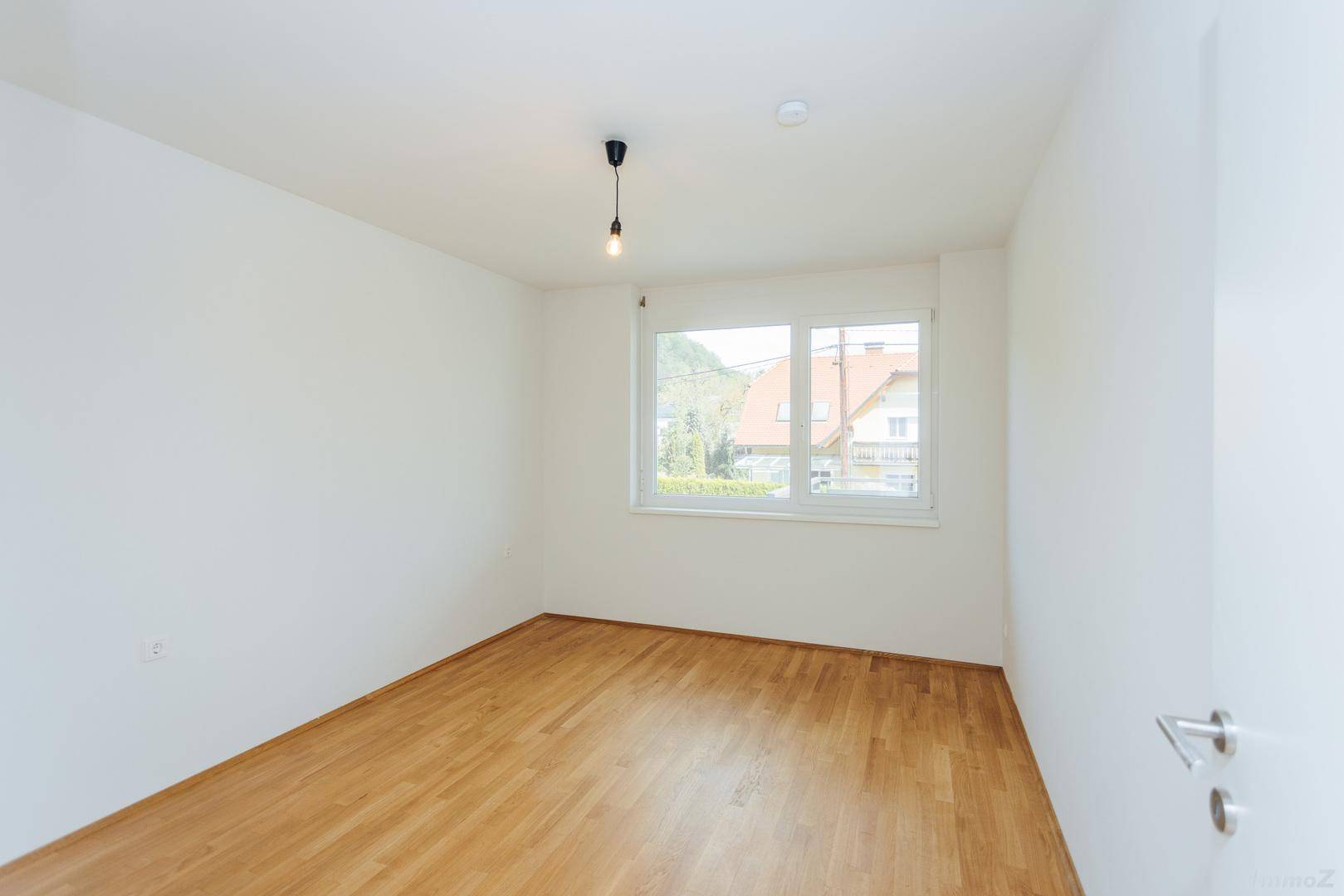 Heller, leerer Raum mit Holzboden und Fenster, das einen Blick auf die Umgebung bietet.