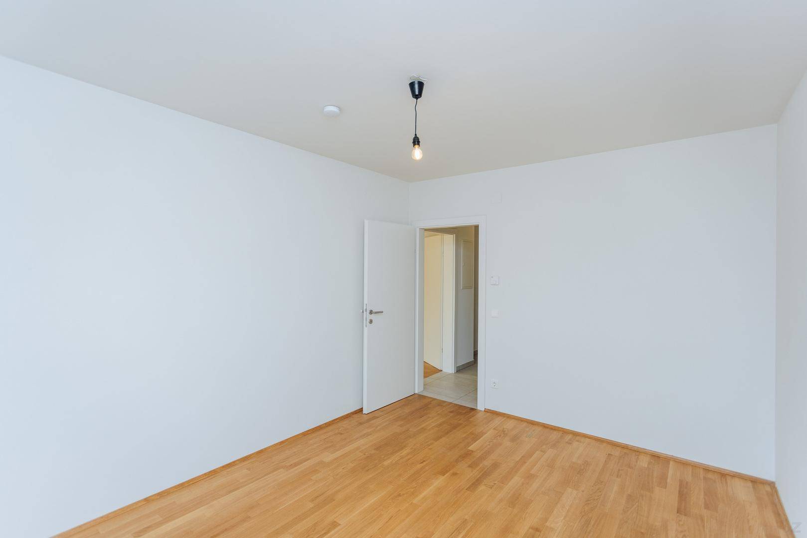 Leerer Raum mit hellem Holzboden und weißen Wänden, bereit zur individuellen Gestaltung.