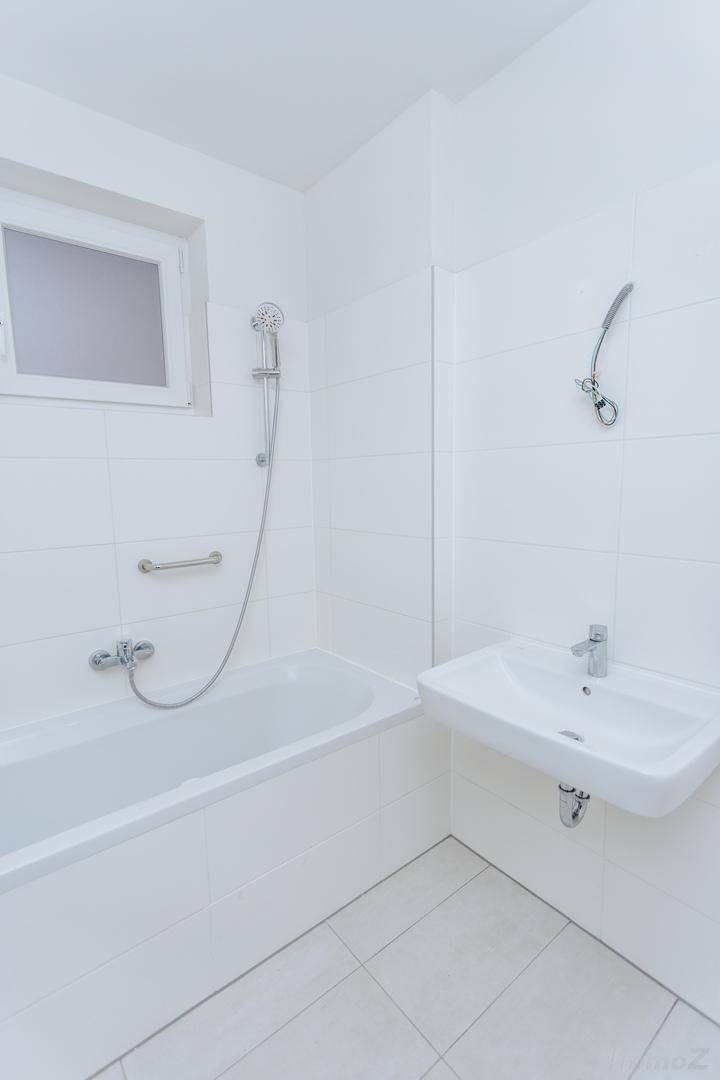 Modernes Badezimmer mit weißen Fliesen, Badewanne mit Duschvorrichtung und einem einzelnen Waschbecken.