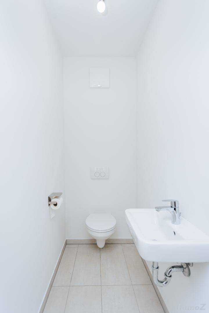 Modernes Gäste-WC mit wandhängender Toilette, kleinem Waschbecken und Fliesenboden.