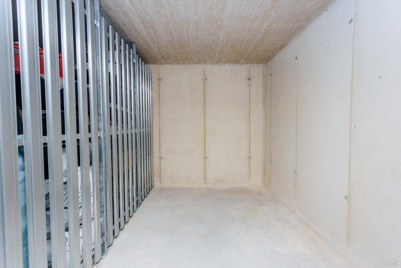 Geräumiger Abstellraum im Keller mit Betonwänden und Metallabtrennungen für zusätzlichen Stauraum.