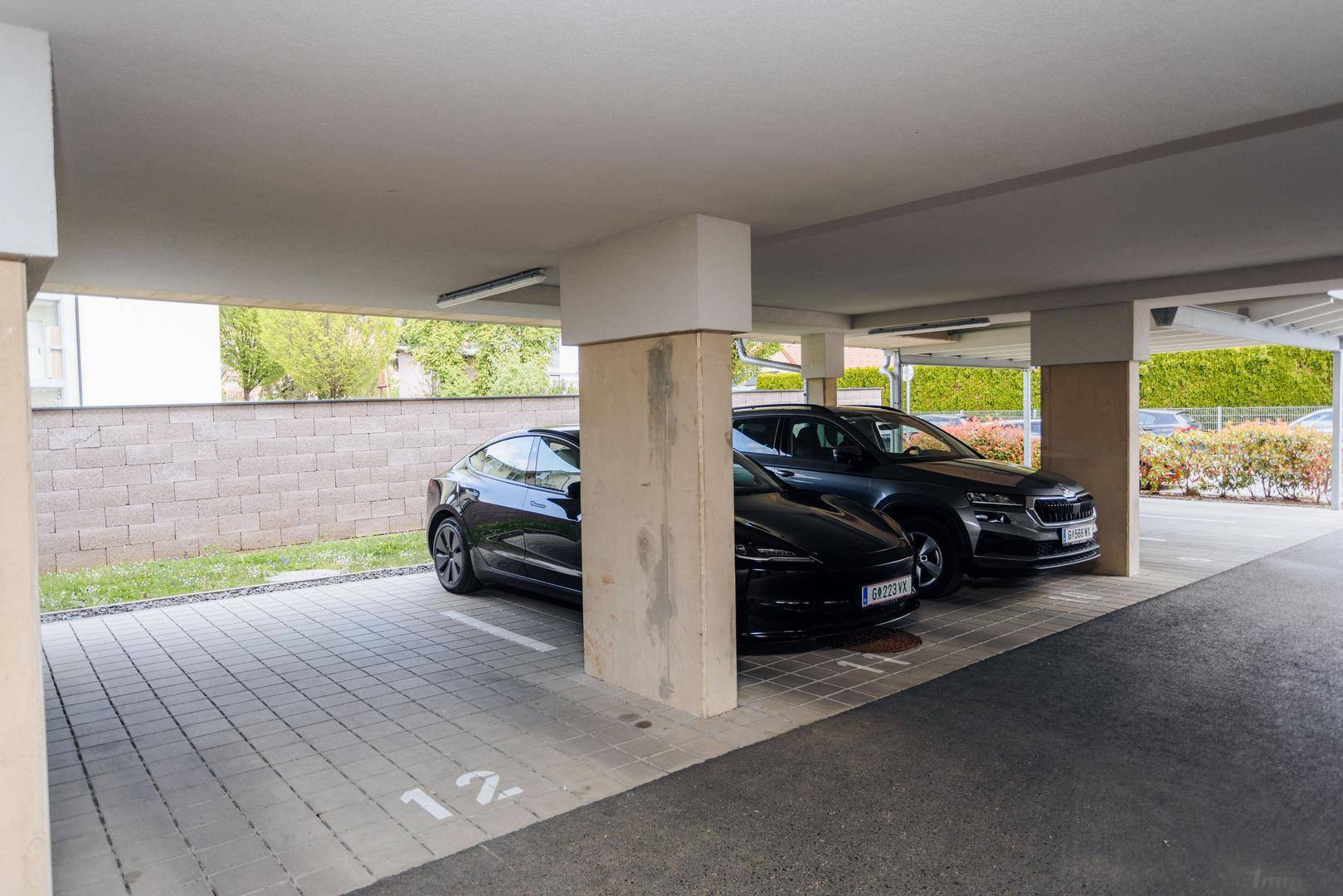 Überdachter Außenparkplatz mit zwei Stellplätzen und gepflastertem Boden.