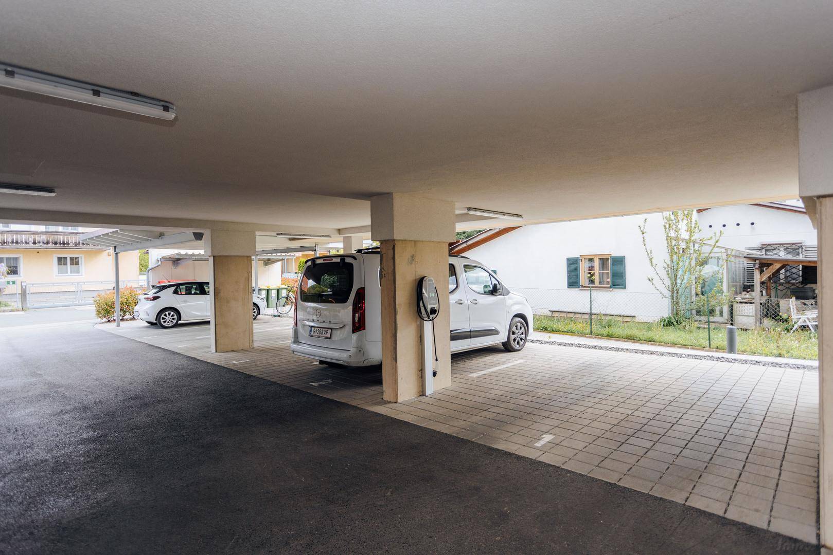Überdachter Außenparkplatz mit Ladestation für Elektrofahrzeuge und gepflastertem Boden.