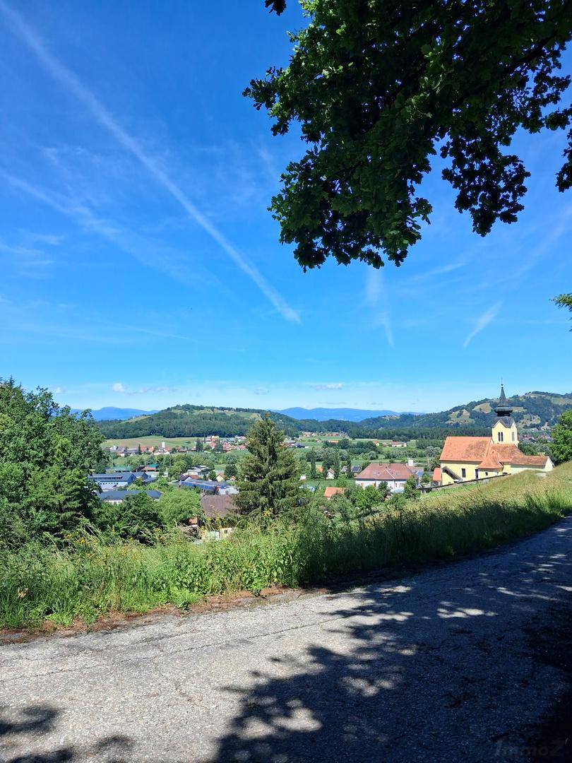 Weitläufiger Panoramablick auf ein idyllisches Dorf mit Kirche und die hügelige Landschaft.