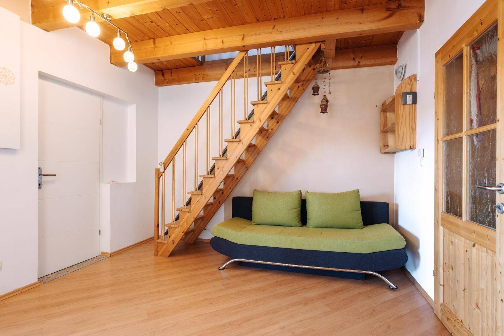 Gemütlicher Wohnbereich mit Holzbalkendecke, Holztreppe und einem Sofa.