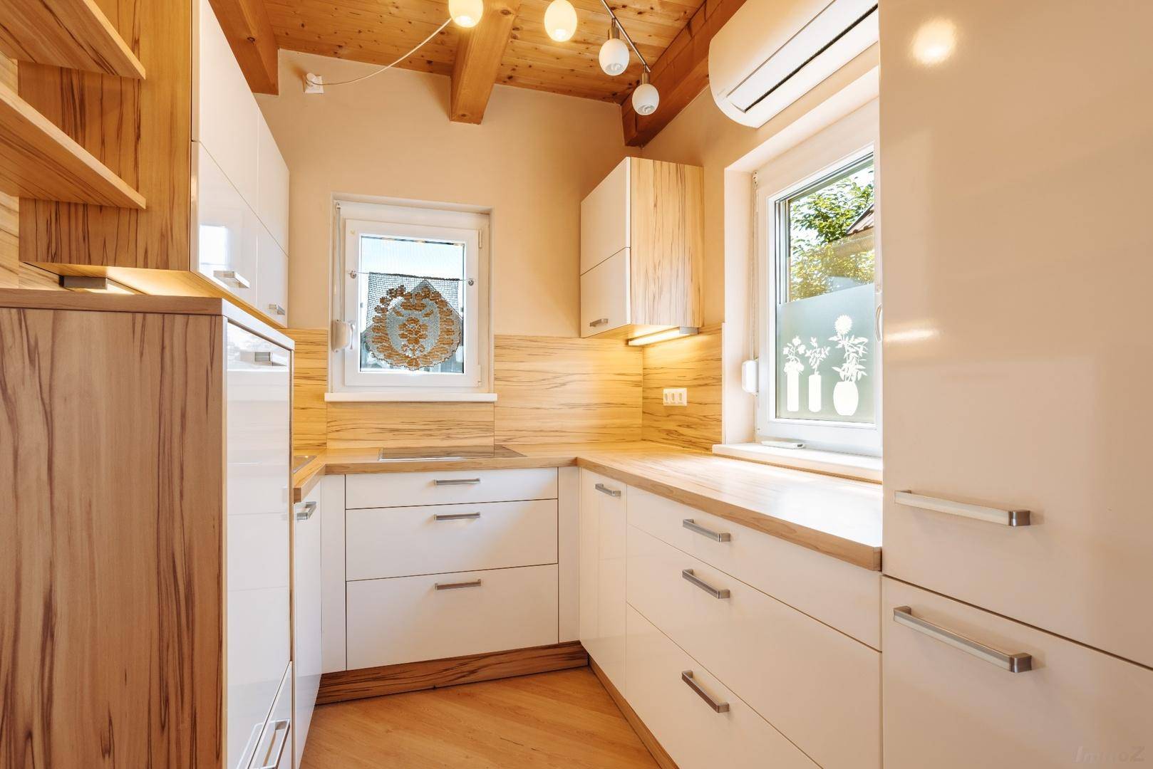 Moderne Küche mit weißen Hochglanzfronten, Holzarbeitsplatten und sichtbaren Holzbalken an der Decke.