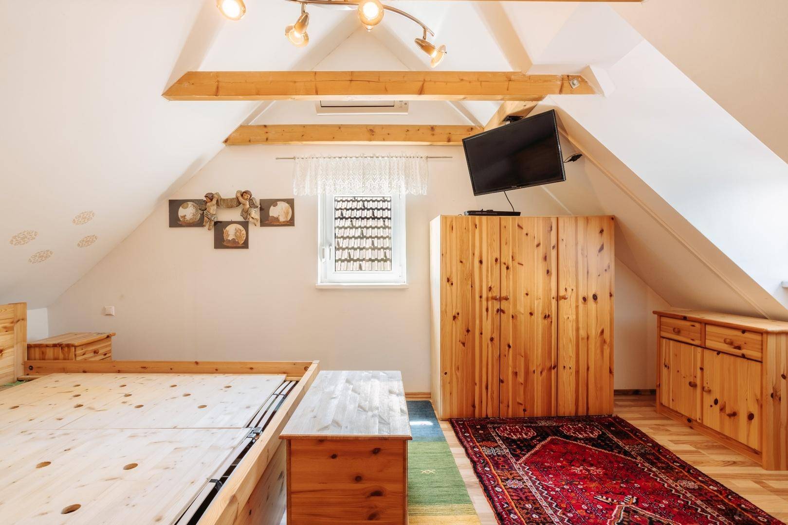 Gemütliches Schlafzimmer im Dachgeschoss mit Holzbalken, schrägen Wänden und traditionellem Teppich.