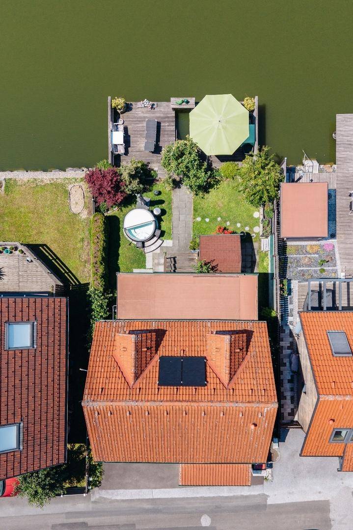 Senkrechte Luftaufnahme des Grundstücks mit Haus, Garten, Whirlpool und Holzterrasse am See.