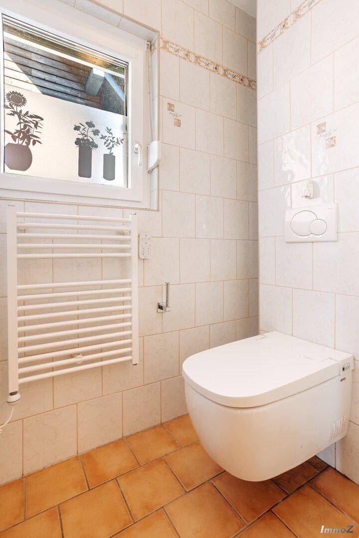 Badezimmer mit Toilette, Waschbecken und beheiztem Handtuchhalter, hell gefliest.