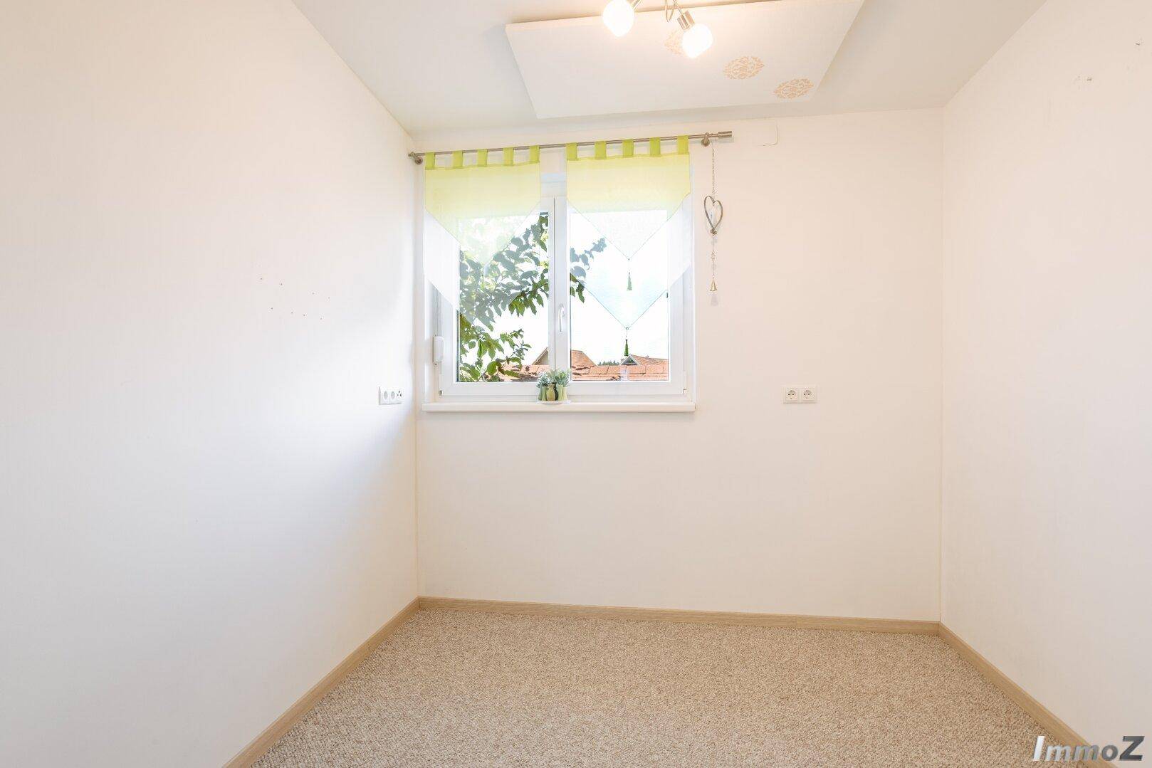 Helles Zimmer mit weiß gestrichenen Wänden und einem Fenster mit Blick ins Grüne.