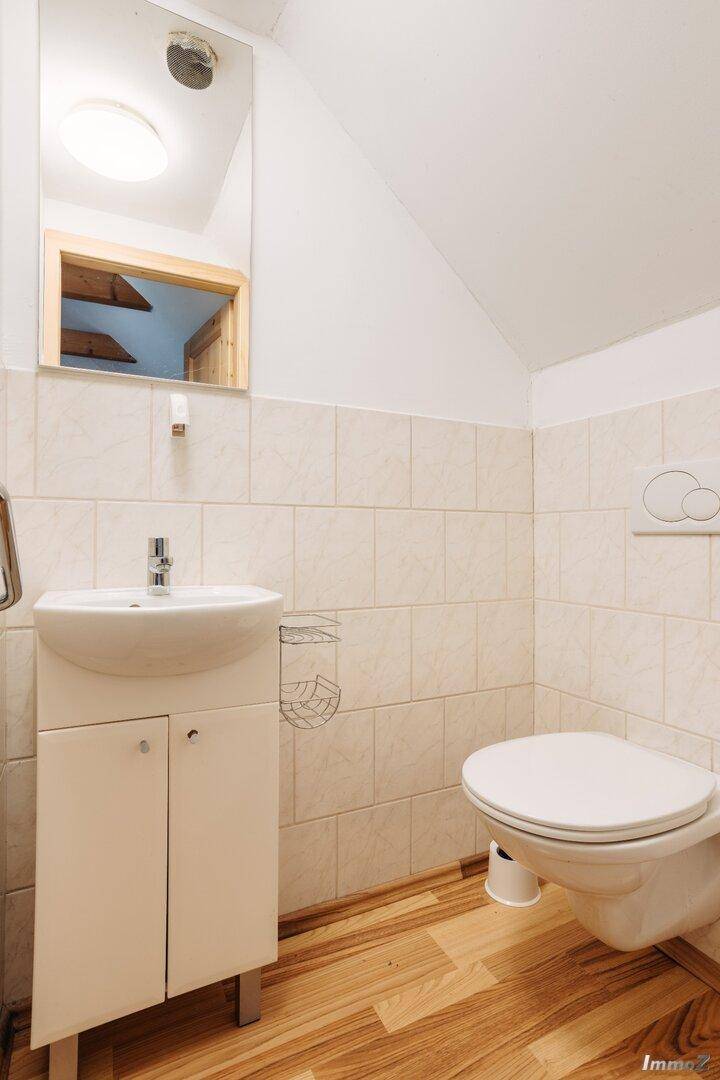 Kleines WC mit Waschbecken, Toilette und hellen Fliesen an den Wänden.