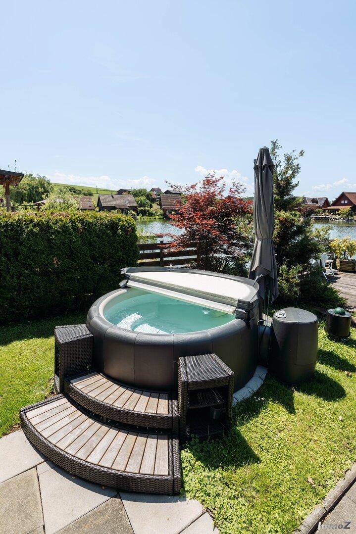Entspannender Whirlpool im Gartenbereich mit Holzstufen und Blick auf den See im Hintergrund.