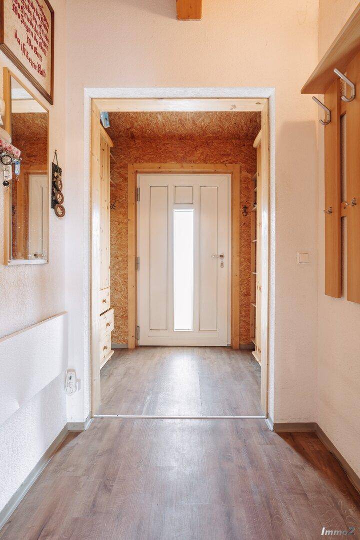 Heller Eingangsbereich mit Holzboden und Garderobe, führt zu einer weißen Eingangstür.