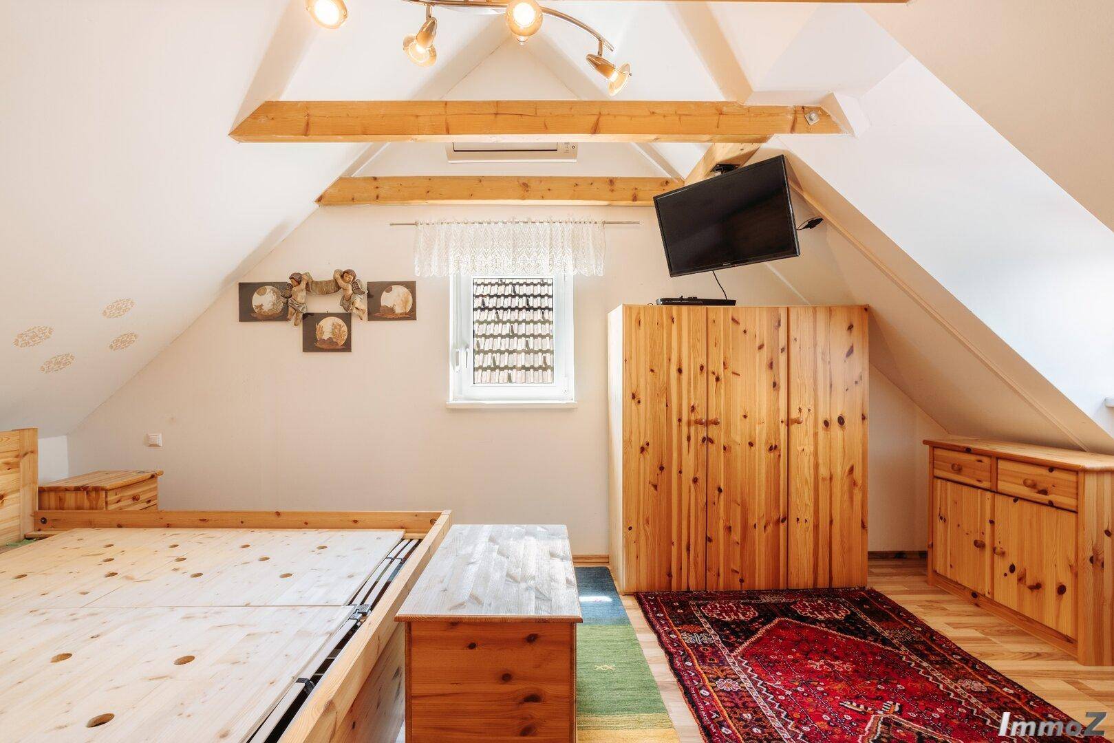 Gemütliches Schlafzimmer im Dachgeschoss mit Holzbalken, Holzbett und Teppichboden.