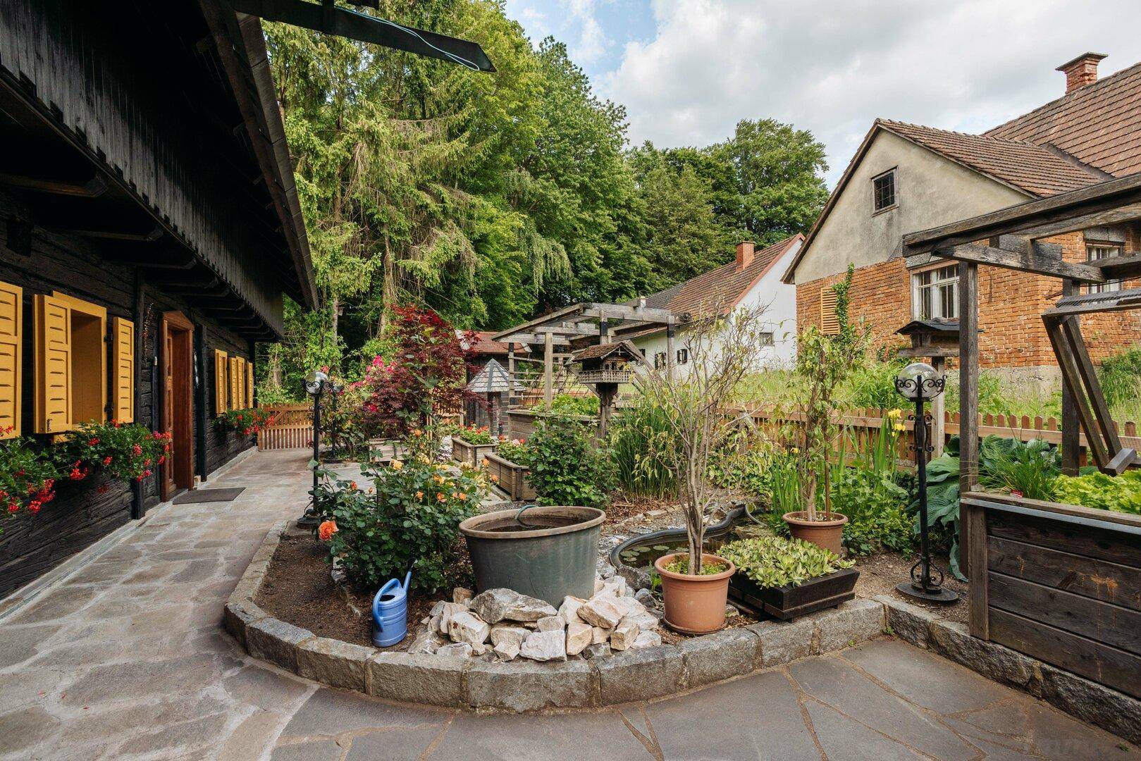 Gepflegter Gartenbereich mit Steinwegen, Blumenbeeten und einem kleinen Teich neben dem Haus.