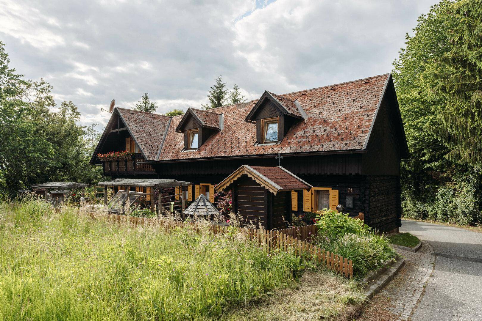 Traditionelles Holzhaus mit rotem Ziegeldach und Gaubenfenstern in ländlicher Umgebung.