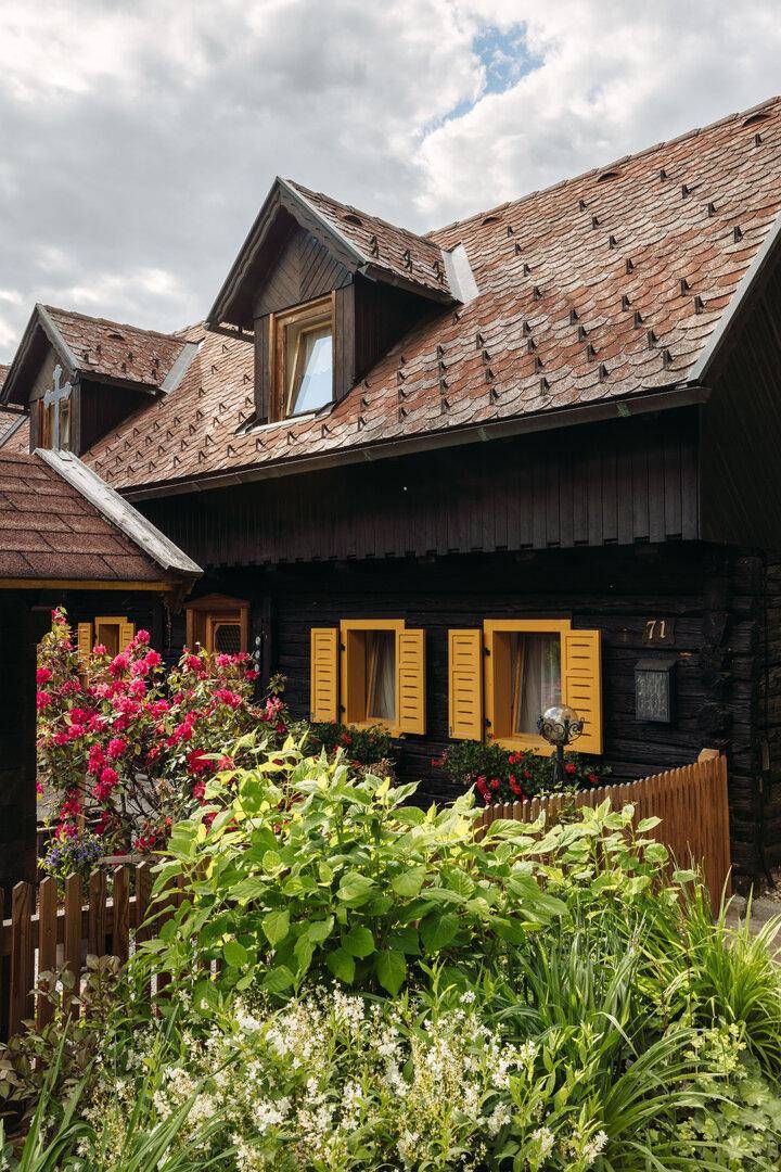 Charmantes Holzhaus mit gelben Fensterläden und blühenden Sträuchern im Vorgarten.