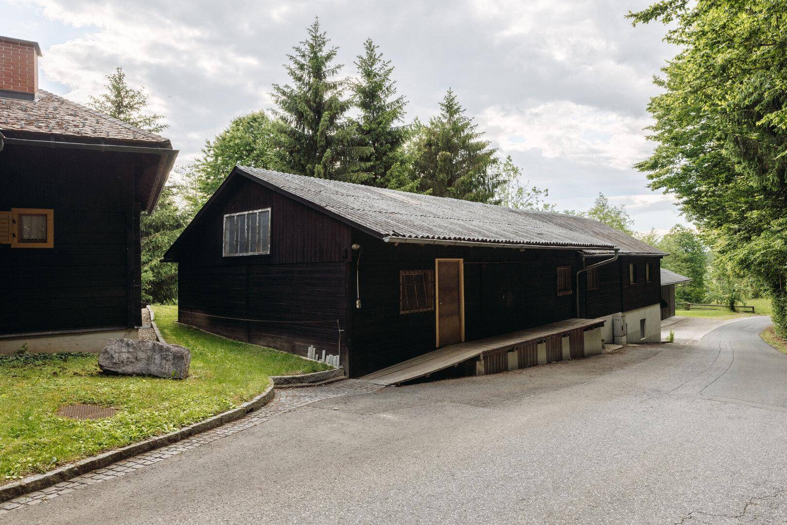 Langes Nebengebäude mit Holzfassade und Rampe, umgeben von Bäumen.