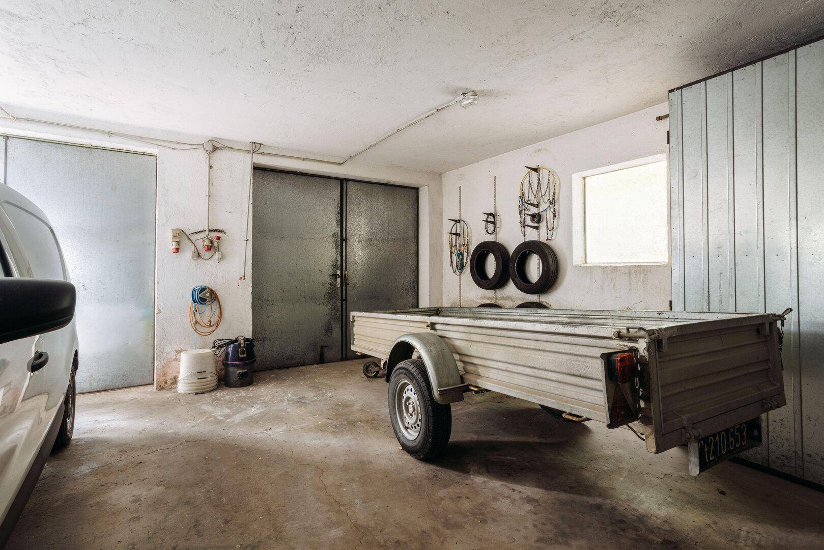 Geräumige Garage mit Betonboden, Metalltoren und Anhänger.