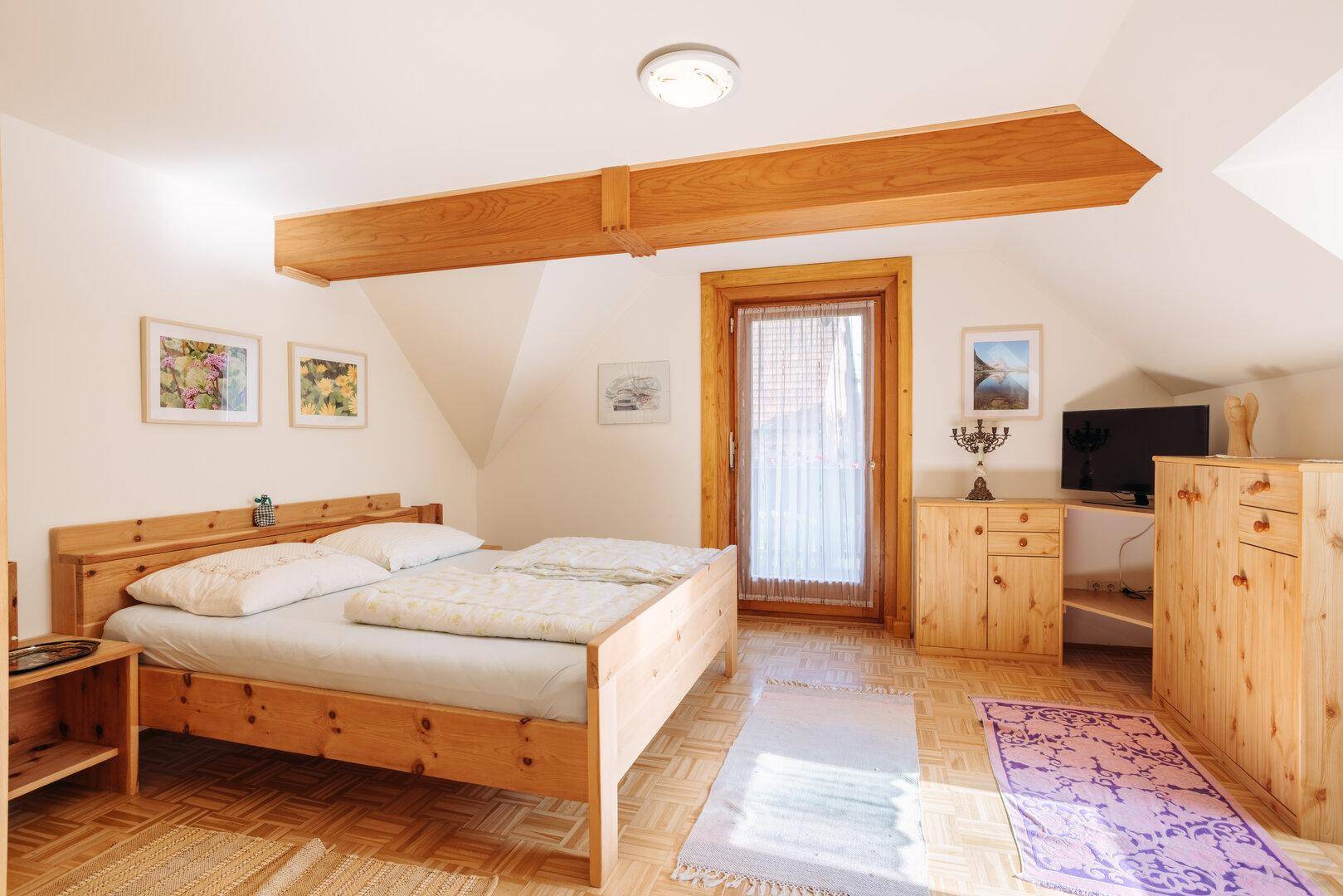 Helles Schlafzimmer mit Holzbalken, Doppelbett und Parkettboden.