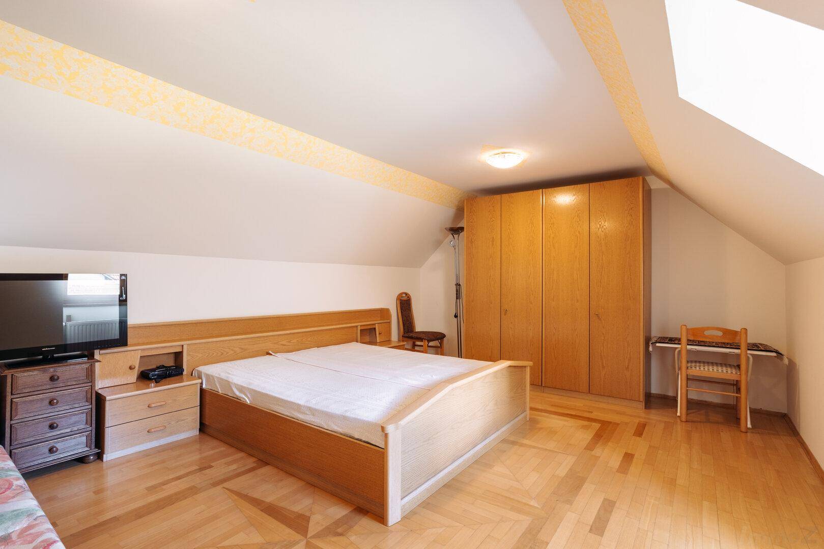 Geräumiges Schlafzimmer im Dachgeschoss mit Doppelbett, Schränken und Parkettboden.