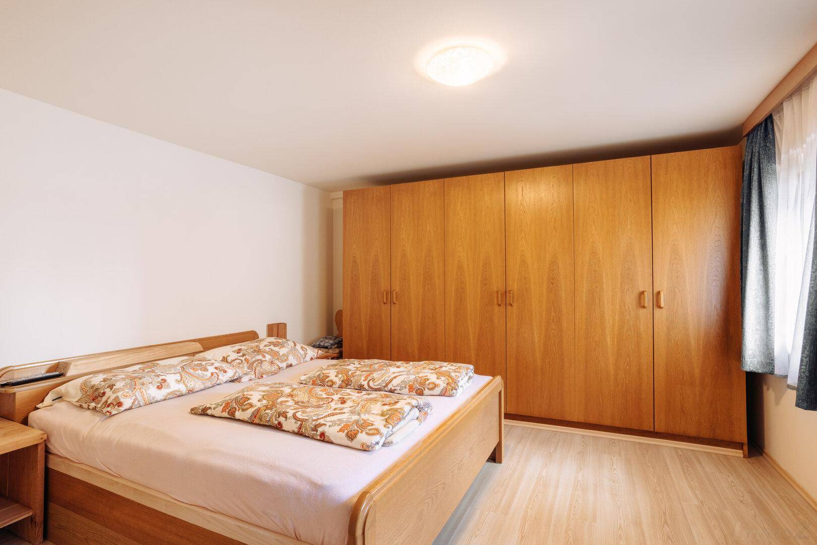 Schlafzimmer mit Doppelbett, großem Kleiderschrank und Laminatboden.