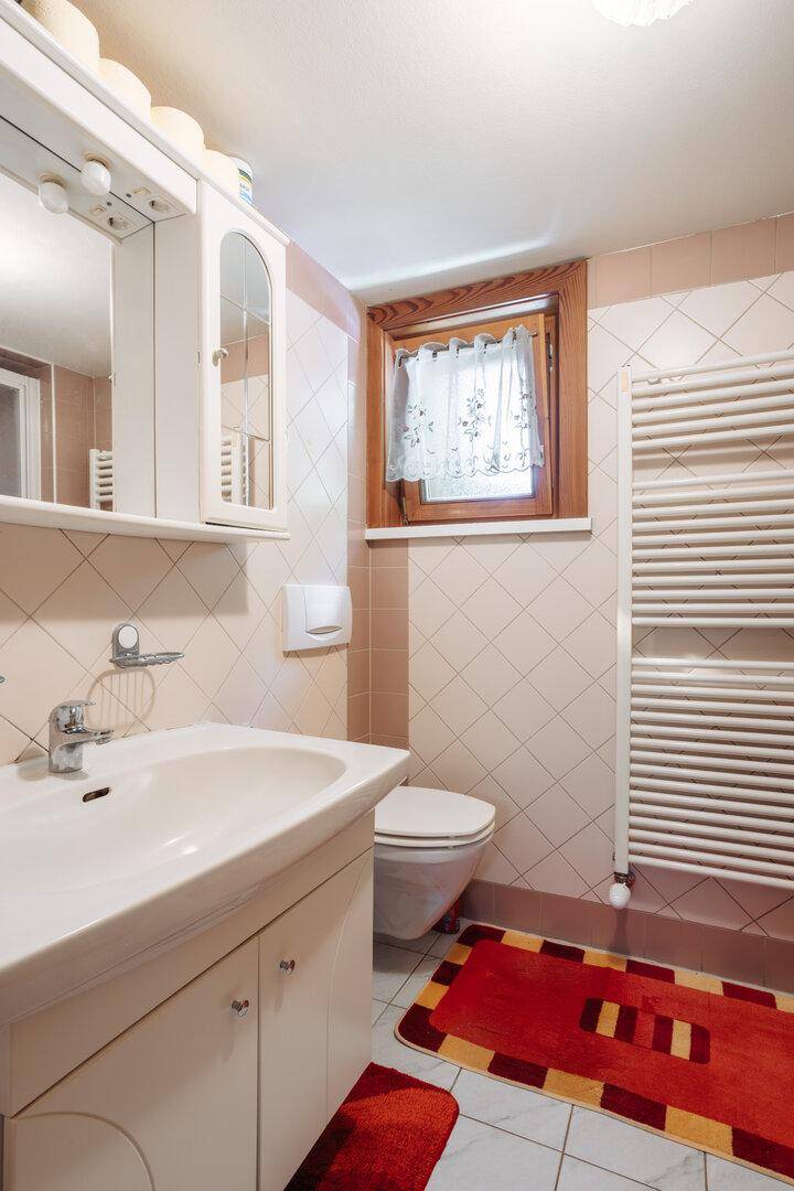 Helles Badezimmer mit Waschbecken, WC, beheiztem Handtuchhalter und Fenster.