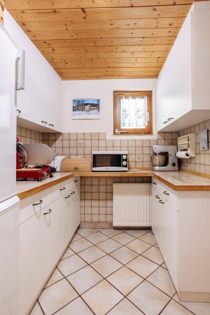 Helle Küchenzeile mit weißen Schränken, Holztheke und gefliestem Boden.