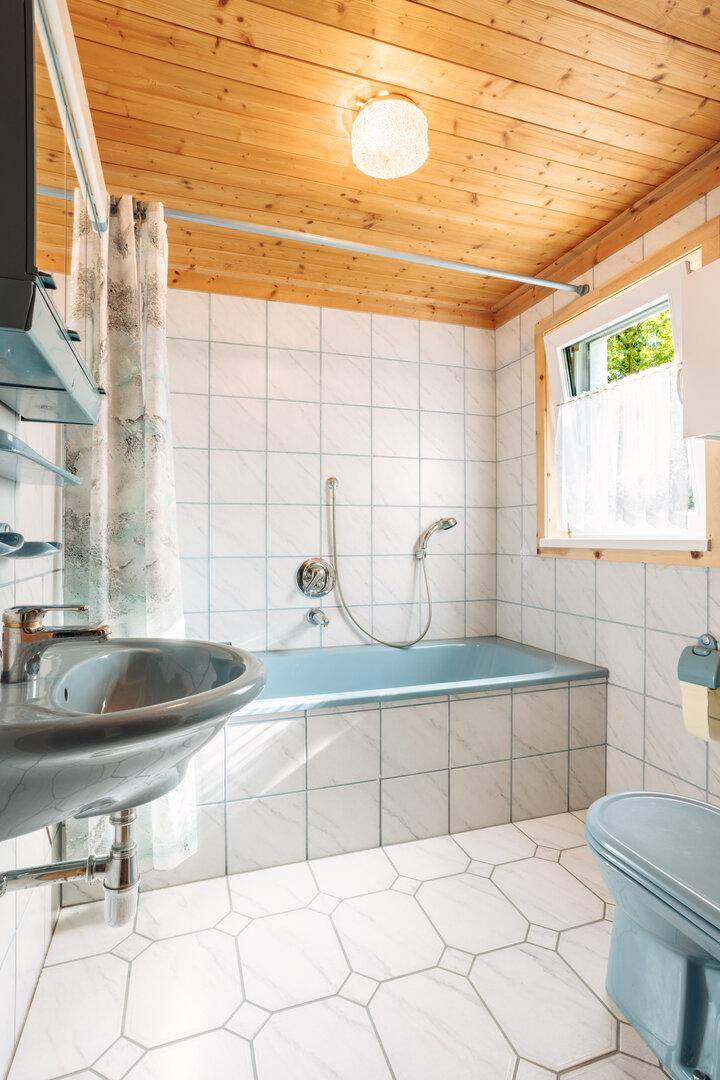 Badezimmer mit blauer Badewanne, weißen Fliesen und Holzdecke.