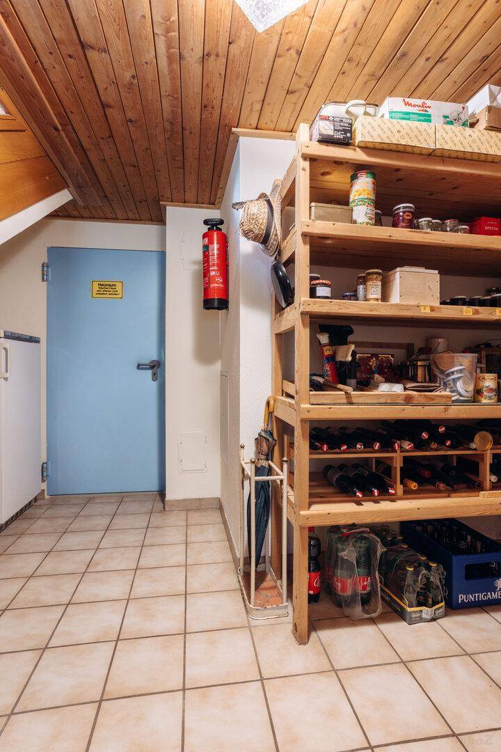 Lagerraum im Keller mit Fliesenboden, Holzregalen und Weinflaschen.