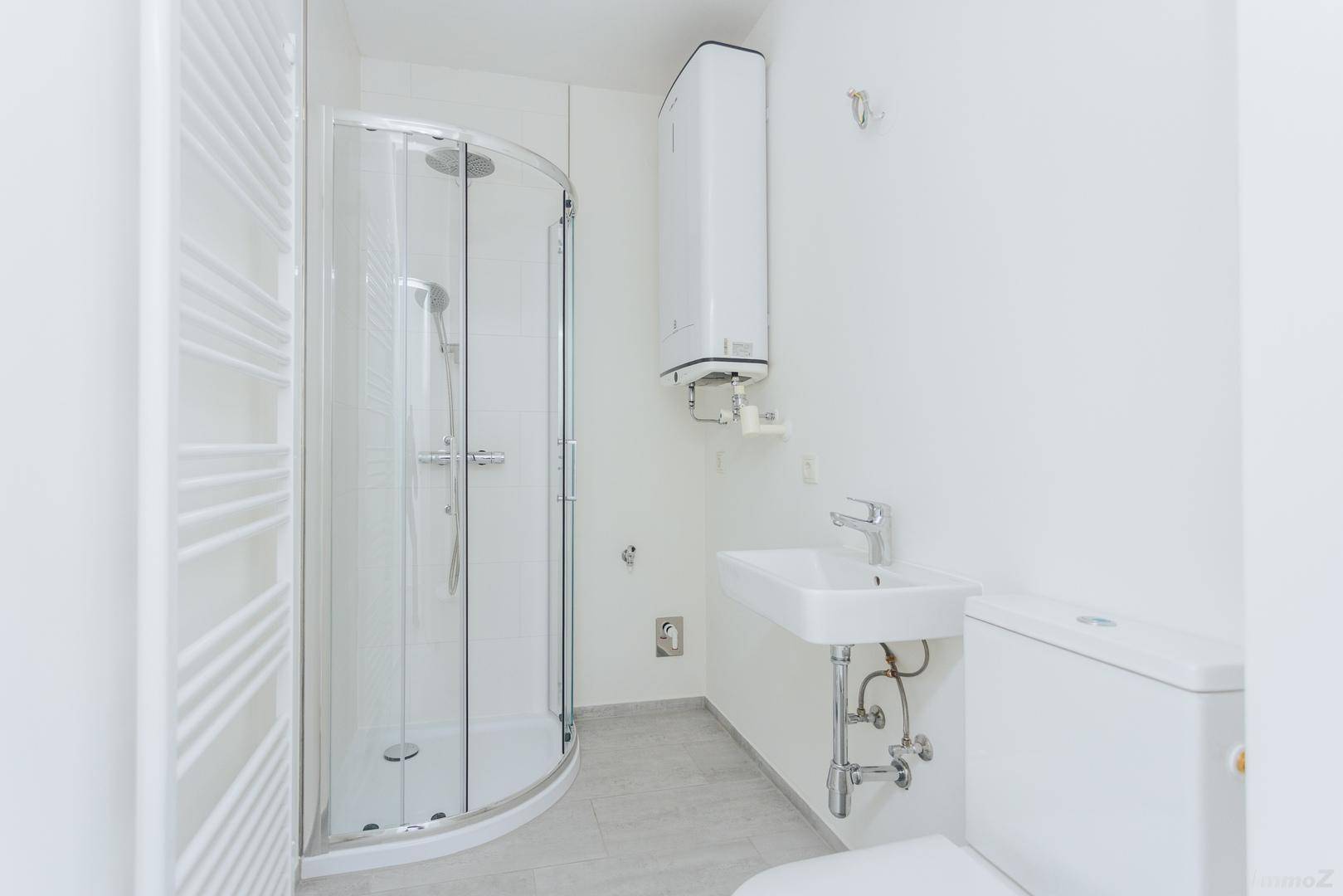 Helles Badezimmer mit Eckdusche, Waschbecken, WC und Handtuchheizkörper, bereit zur Nutzung.