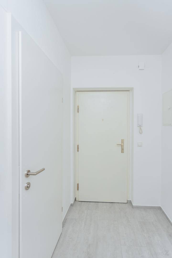 Heller Eingangsbereich mit weißer Tür, Fliesenboden und Gegensprechanlage.