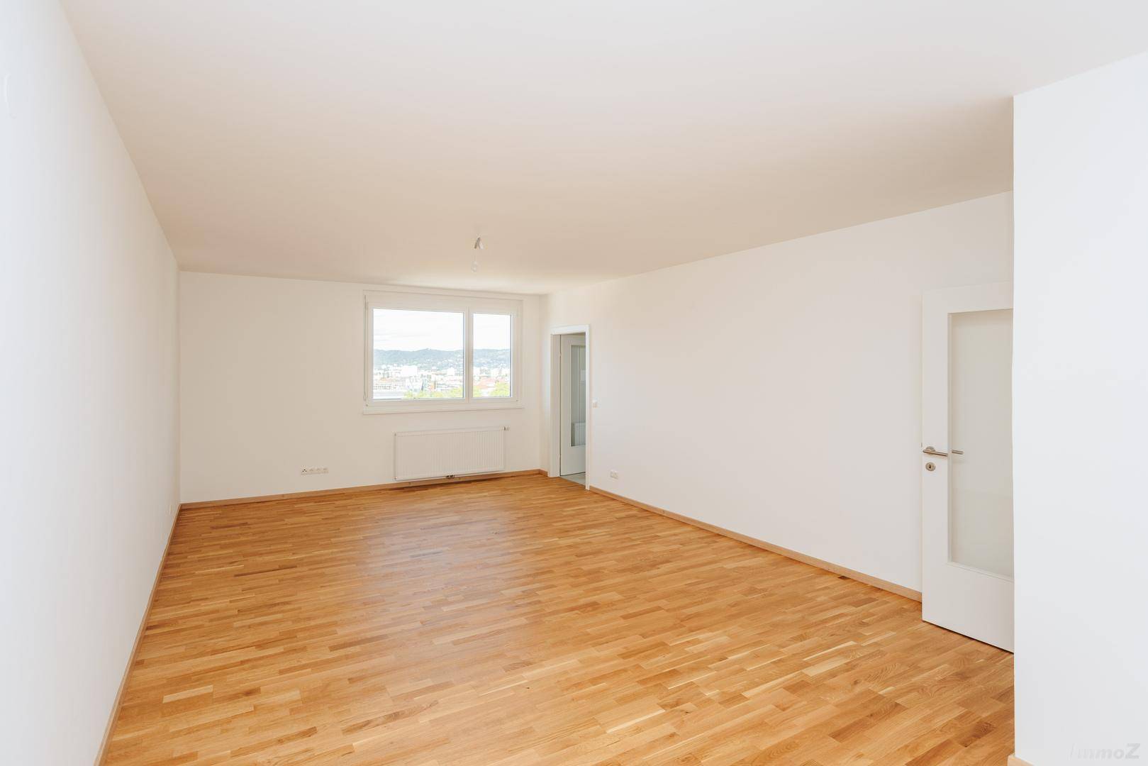 Heller, leerer Raum mit Parkettboden und Fenster, das einen weiten Blick über die Stadt bietet.