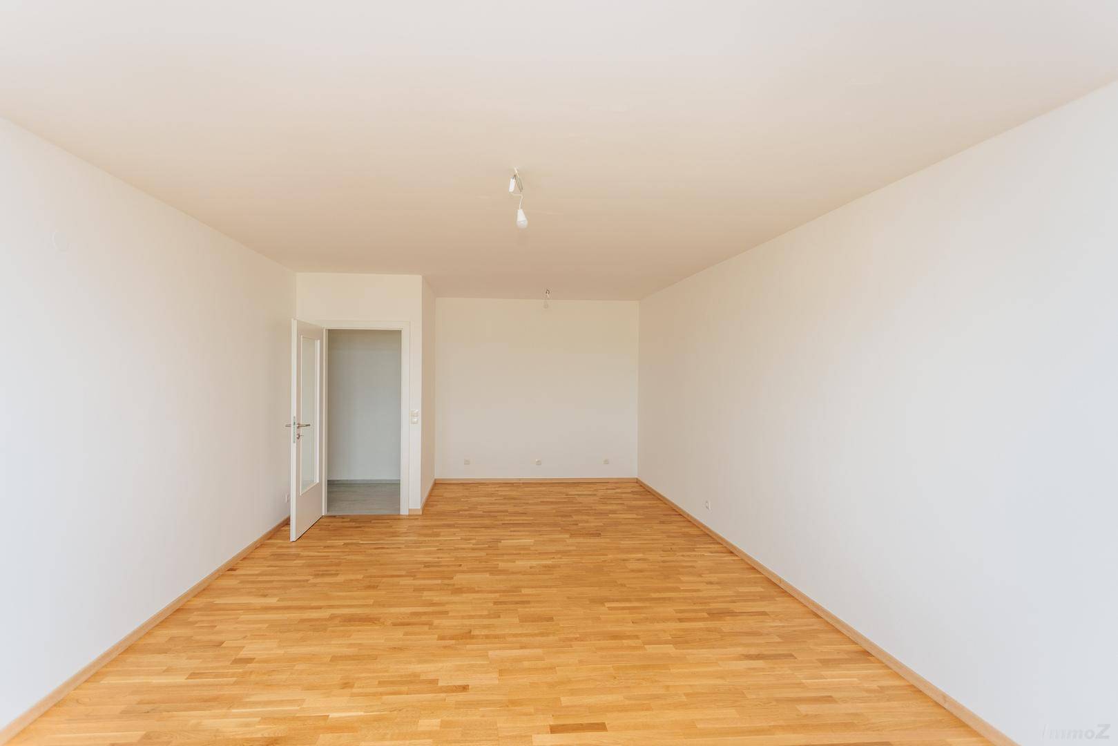Leerer Raum mit hellem Holzboden und weiß gestrichenen Wänden, bereit zur individuellen Gestaltung.