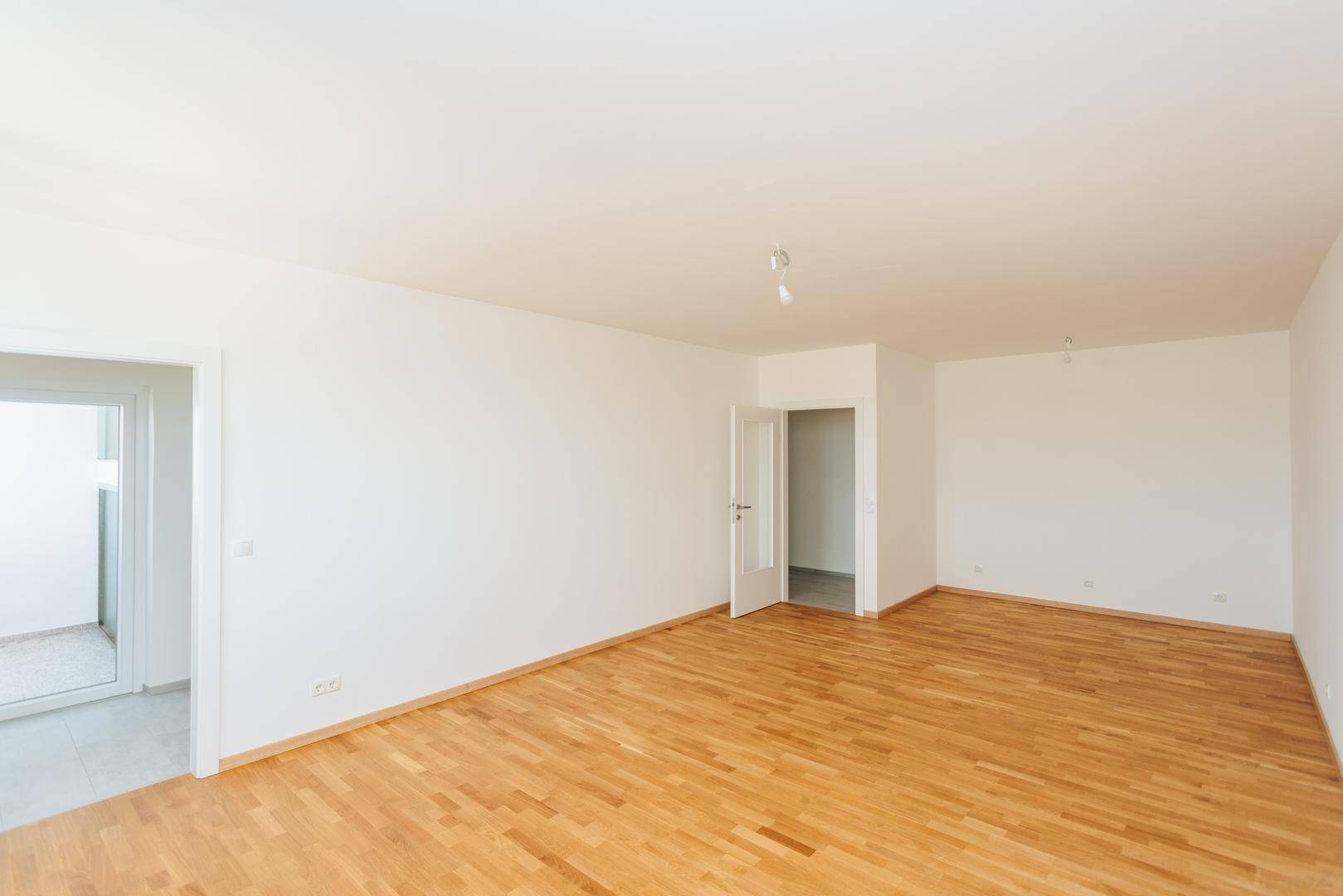 Geräumiger, leerer Raum mit Parkettboden und zwei Türen, die zu weiteren Bereichen führen.