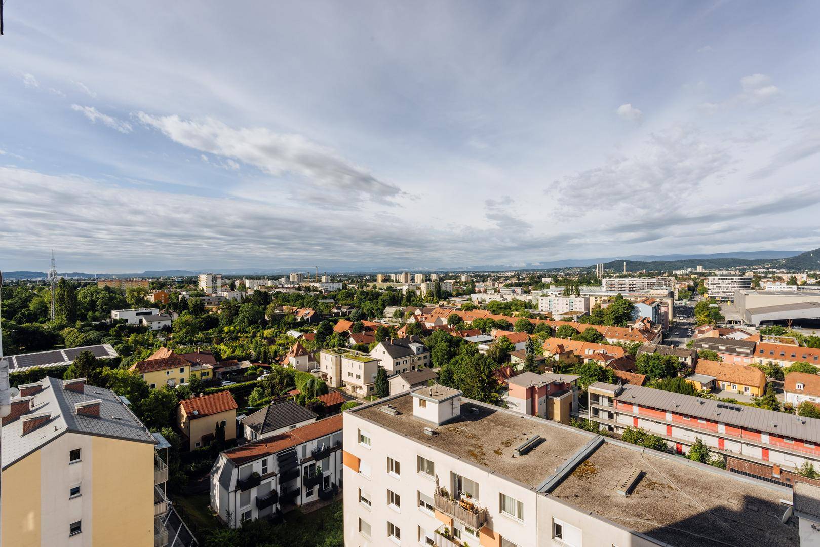 Weiter Blick vom Balkon über die Stadt mit vielen Bäumen und Häusern unter bewölktem Himmel.