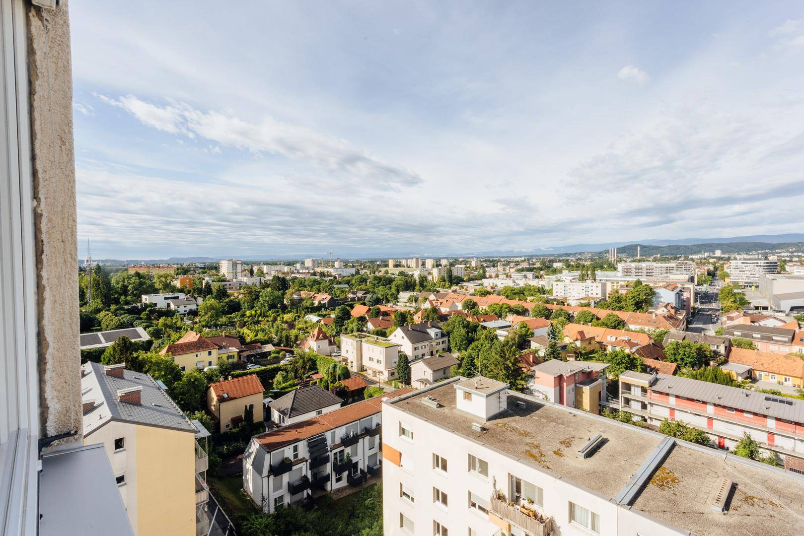 Panoramablick vom Balkon über eine weitläufige Stadtlandschaft mit viel Grün und Bergen im Hintergrund.