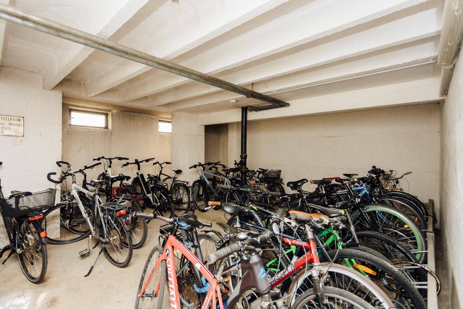Geräumiger Fahrradraum im Untergeschoss mit vielen Fahrrädern und Betonwänden.