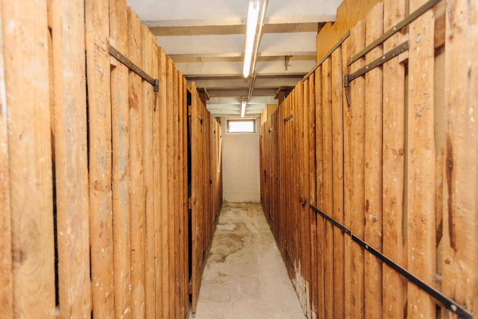 Langer Kellergang mit individuellen Lagerabteilen aus Holz und einfacher Beleuchtung.