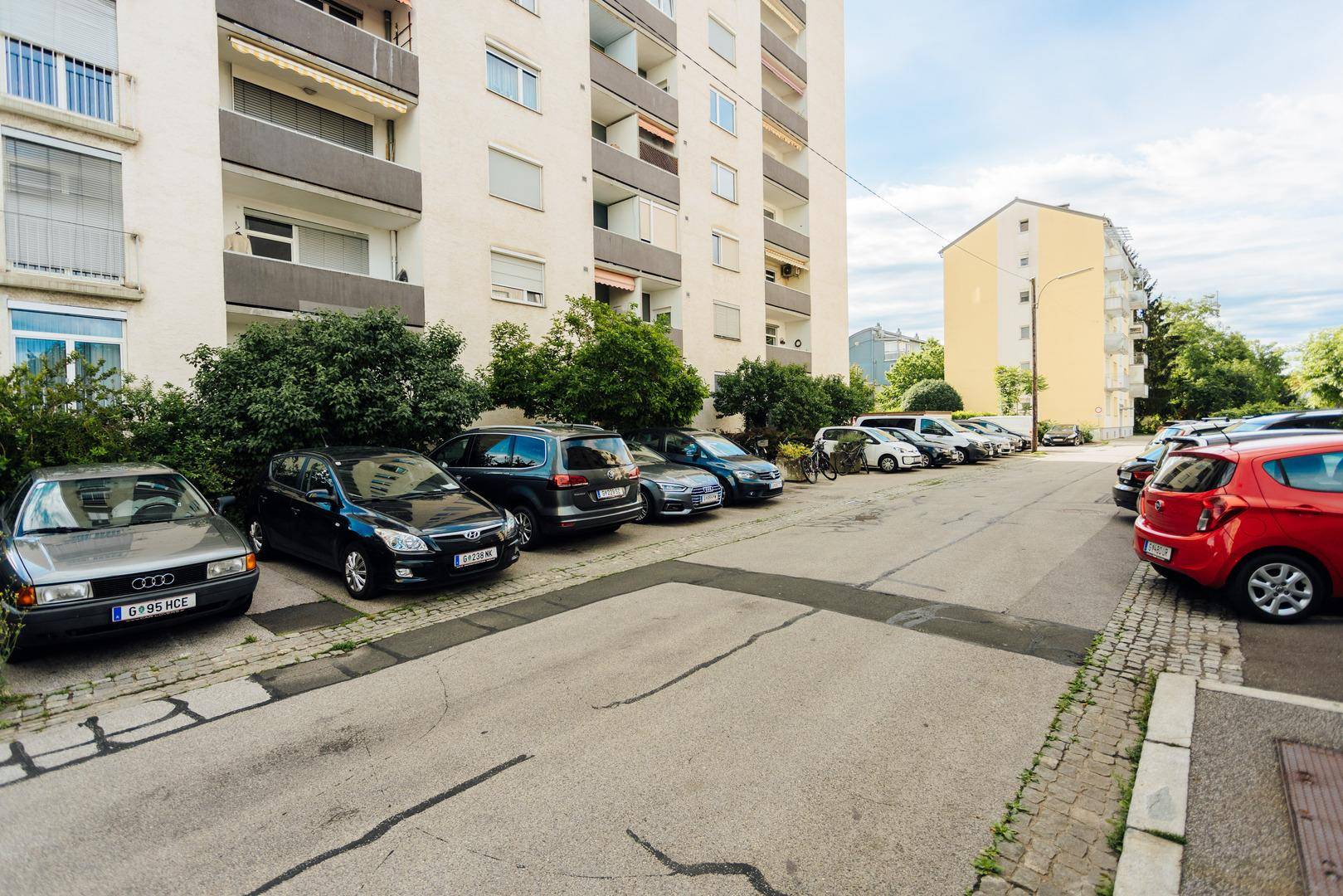 Mehrfamilienhaus mit zahlreichen Parkplätzen vor dem Gebäude und Balkonen an der Fassade.
