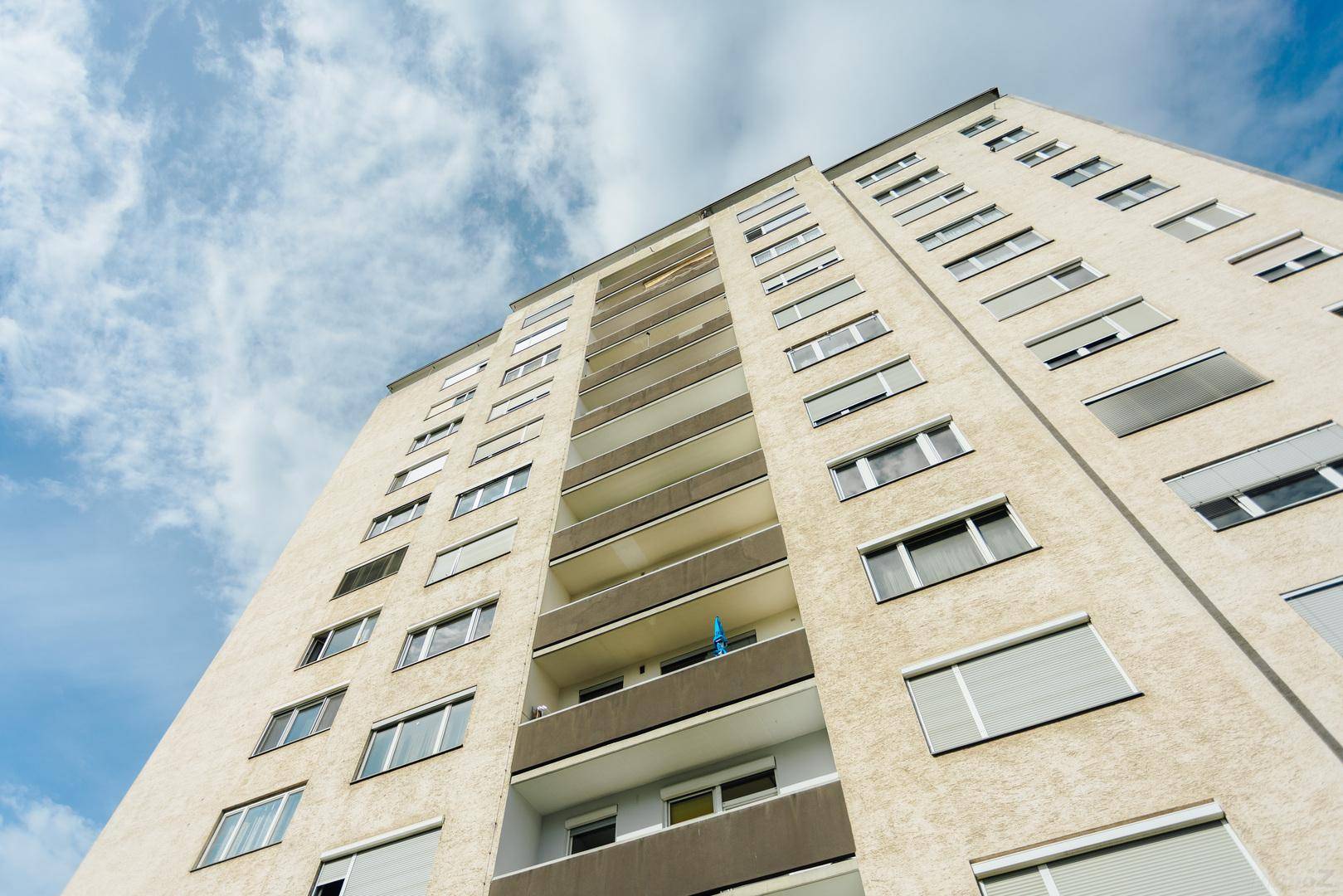 Hohes Wohngebäude mit vielen Etagen und Balkonen unter einem blauen Himmel mit Wolken.