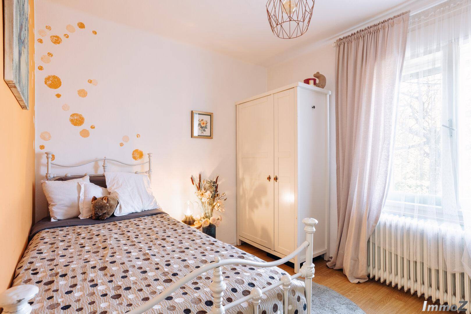 Helles Schlafzimmer mit Einzelbett, Holzboden und dekorativer Wandgestaltung.