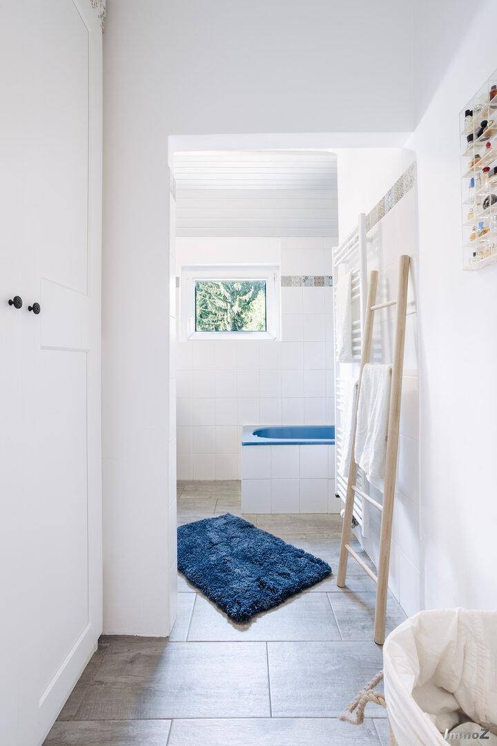 Helles Badezimmer mit blauer Badewanne, weißen Fliesen und Holzdecke.