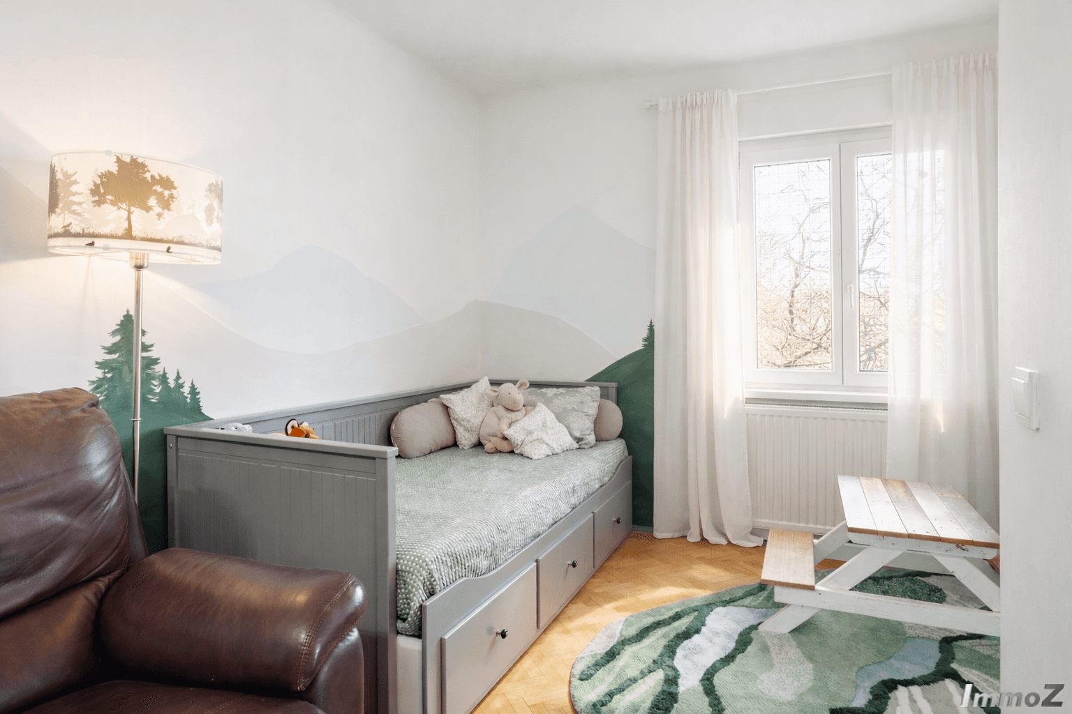 Kinderzimmer mit Tagesbett, Holzboden und Wandmalerei im Bergmotiv.