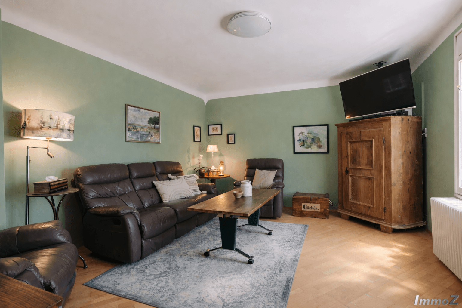 Gemütliches Wohnzimmer mit grünen Wänden, Ledersofa und Parkettboden.